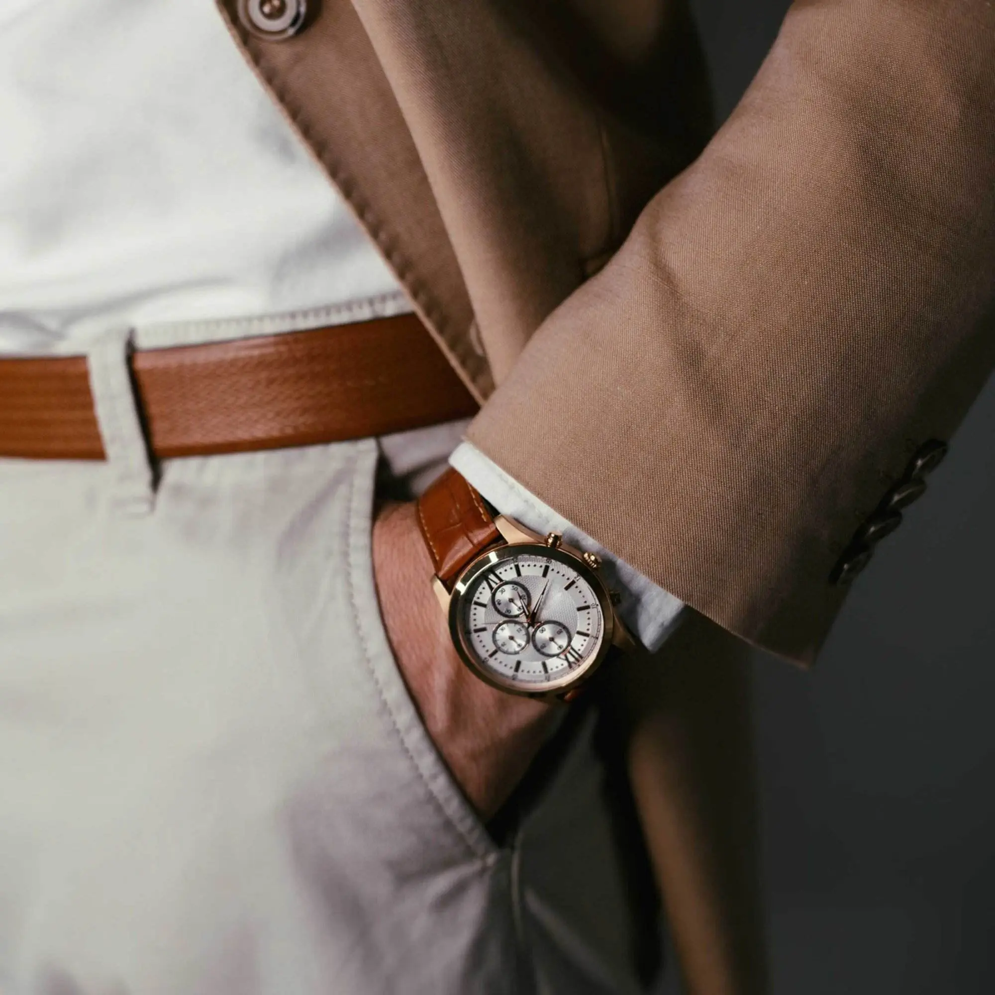 A close-up view shows a gentleman wearing tan pants, a brown wristwatch, a white button-up shirt, and a brown jacket.
